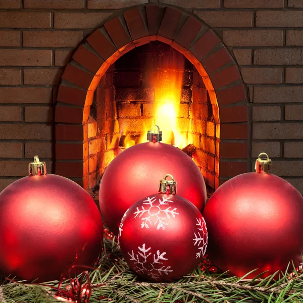 Red Xmas baubles on spruce tree with fireplace — Stock Photo, Image