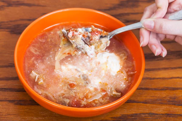 spoon with cabbage soup in hand over ceramic bowl