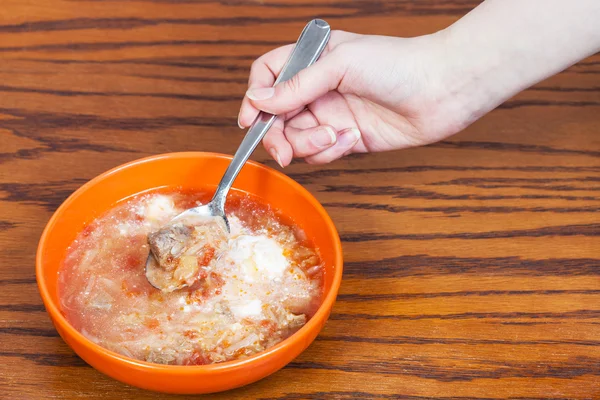 Tangan memegang sendok dengan sup kubis di atas mangkuk — Stok Foto