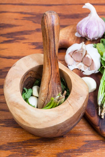 Mortero de madera con cilantro y ajo en la mesa — Foto de Stock