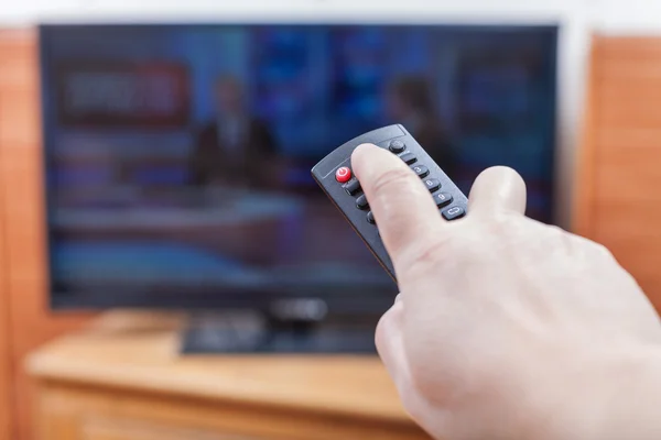 Hand turns on News on TV by remote control — Stock Photo, Image