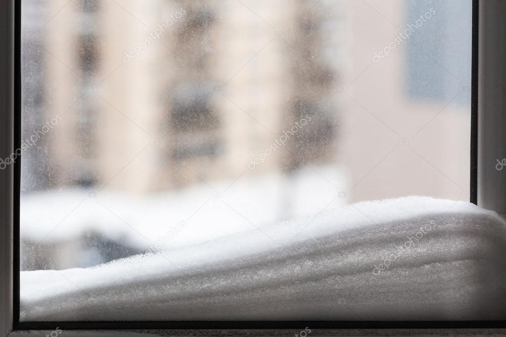 snow on window pane and houses on background