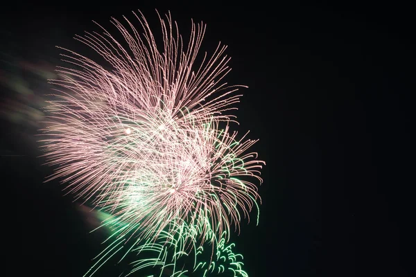 Groen en roze vuurwerk in de nachtelijke hemel — Stockfoto