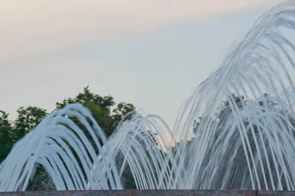 Jets van het water in de fontein op achtergrond van hemel en bomen — Stockfoto
