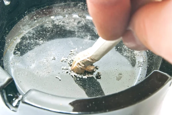 Hand extinguishes his cigarette in dirty ashtray — Stock Photo, Image