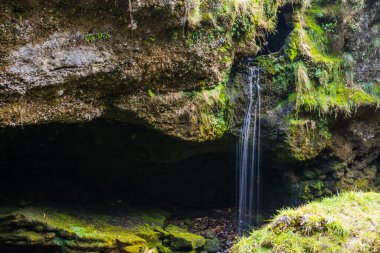 Biraz narin şelale ve dağlarda yeşil bitkilerle birlikte büyük kayalar.