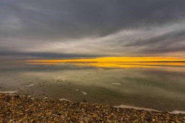 Kışın bulutlu ve güneşli donmuş bir gölün kıyısında taşlarla