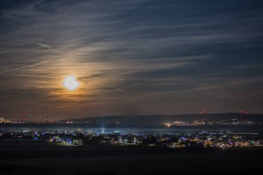 Aydınlanmış şehir, parlak ay ve gece gökyüzünde bulutlar.