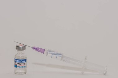 Şişe içinde virüse karşı kapak aşısı sağ arka planda, tam bir şırınga görüşü var.