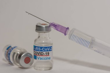 Virüse karşı iki şişe Covid aşısı ve gri arka planı olan bir şırınga.