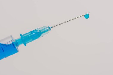 Mavi sıvı aşılı bir şırınga ve ön tarafta beyaz arka planda bir damla.