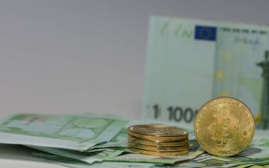 Bir tanesi arka planda 100 Euro 'luk banknotların üzerinde duran bir yığın bitcoin' in yanında duruyor.