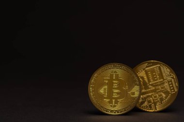 Önü ve arkası siyah arka planı olan iki altın parlaklığında değerli bitcoin.