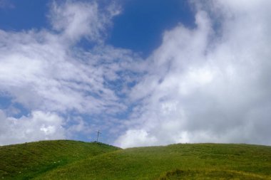 Zirvesi olan yeşil tepeler ve yürüyüş yaparken beyaz bulutlar.