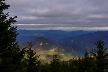 Güneşteki yumuşak yeşil dağlar ve yoğun bulutlu gri gökyüzü
