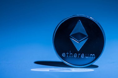 Mavi ışıkla aydınlatılmış ethereum madeni para ve yansımalı gölge.