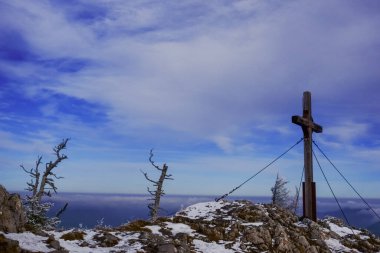 Bir zirve haçı ve kışın mavi gökyüzü olan eğri büğrü ağaç gövdeleri