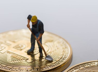 Gri arka plan makro görünümlü altın bir bitcoin üzerinde çalışan tek bir madenci
