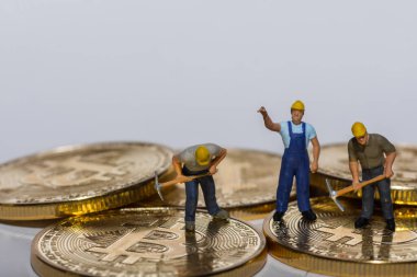 Gri arka planı olan altın parlayan bitcoinler üzerinde çalışan üç madenci.
