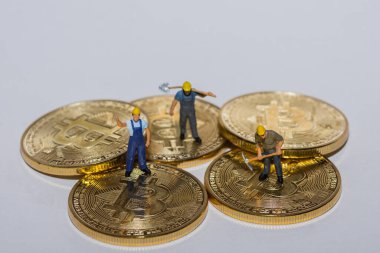 Beş altın sikkenin üzerinde duran üç madenci. Gri arka planı olan kripto para birimi.