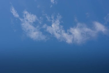 Güneşin altında yürürken mavi gökyüzünde ince beyaz bulutlar