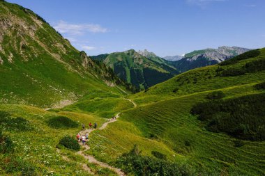 Yazın renkli yürüyüşçülerle yeşil bir dağ manzarasında uzun bir yürüyüş yolu.