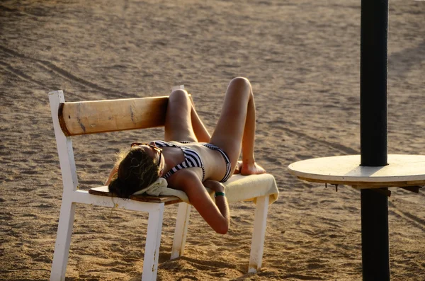 Kvinna i bikini sova på bänken på stranden — Stockfoto