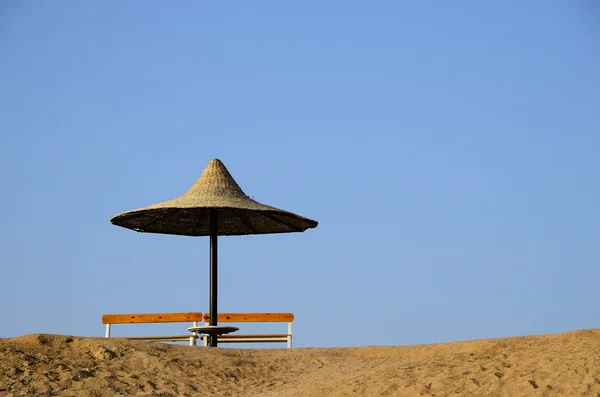 Guarda-chuva de palha e banco na praia — Fotografia de Stock