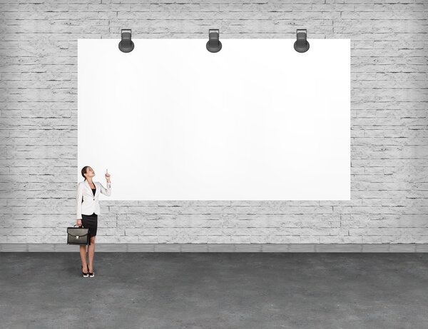 Elegant business woman standing and looking at blank white billboard. Copy-space for advertise.