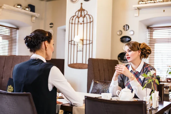 Two pretty girl-friends talk in cafe