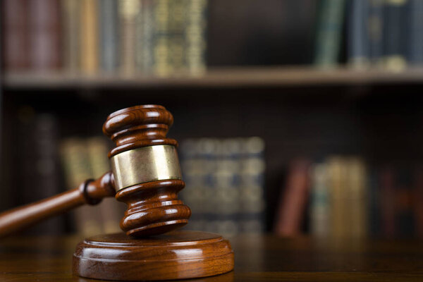 Law theme. Judge chamber. Gavel on brown desk. Collection of legal books in the bookshelf.