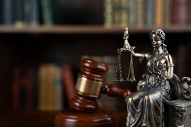 Hukuk ve adalet kavramı. Yargıç odası. Heykel ve hakimler kahverengi masanın üzerinde duruyor. Kitaplıkta yasal kitap koleksiyonu.