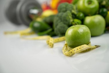 Fitness konsepti. Sağlıklı beslenme: meyve ve sebze. Spor aletleri: tartı makinesi ve dambıllar. Beyaz arkaplan.