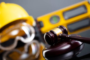 İnşaat hukuku kavramı. Gri arkaplanda miğfer ve hakimler tokmak.