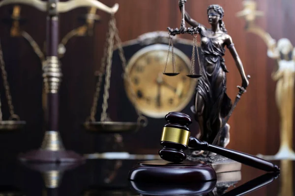 Law concept. Judge wooden gavel, scale, old clock and Themis statue on brown background.