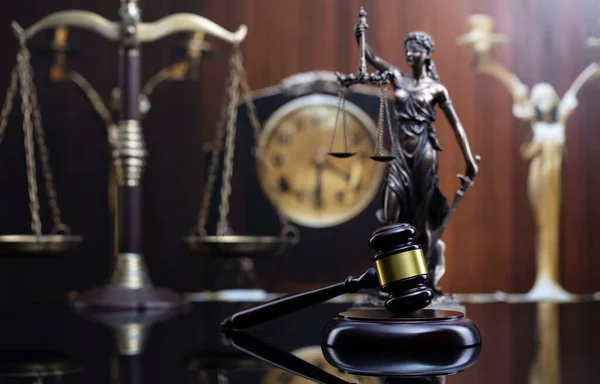 Law concept. Judge wooden gavel, scale, old clock and Themis statue on brown background.