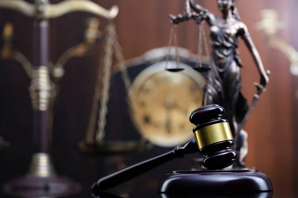 Law concept. Judge wooden gavel, scale, old clock and Themis statue on brown background.