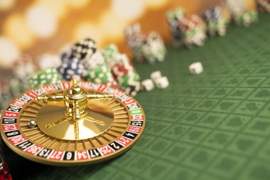 Kumarhane kavramı. Rulet çarkı, poker çipleri ve zarlar yeşil masada ve sarı bokeh arka planda.