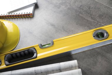 Müteahhit konsepti. Müteahhidin alet çantası, sarı başlık, libella, el testeresi. Gri karoların arka planındaki planlar ve defterler.