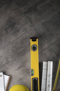 Müteahhit konsepti. Müteahhidin alet çantası, sarı başlık, libella, el testeresi. Gri karoların arka planındaki planlar ve defterler.