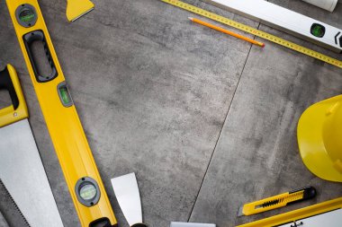 Müteahhit konsepti. Müteahhidin alet çantası: sarı baret, iftiracı, el testeresi arka planda gri kiremitler..