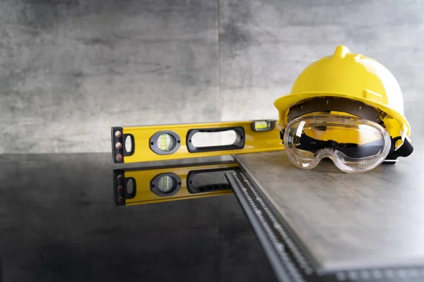 Contractor concept. Tool kit of the contractor: yellow hardhat, libella and tools on the gray background.