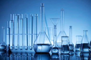 Laboratuvar araştırmaları. Mavi arka planda cam tüpler ve beherler.