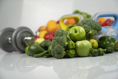 Fitness konsepti. Sağlıklı beslenme: meyve ve sebze. Spor aletleri: tartı makinesi ve dambıllar. Beyaz arkaplan.