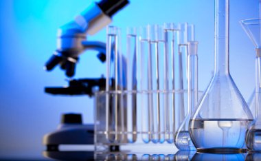 Laboratuvar araştırmaları. Mavi arka planda mikroskop, cam tüpler ve deney tüpleri..