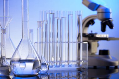 Laboratuvar araştırmaları. Mavi arka planda mikroskop, cam tüpler ve deney tüpleri..