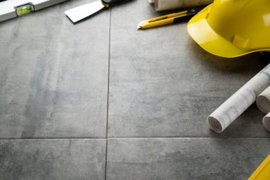 Müteahhit teması. Planlar, müteahhitin alet çantası, sarı başlık ve iftiralar. Gri karolar arka plan.