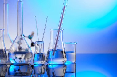 Laboratuvar araştırmaları. Mavi arka planda cam tüpler ve beherler.