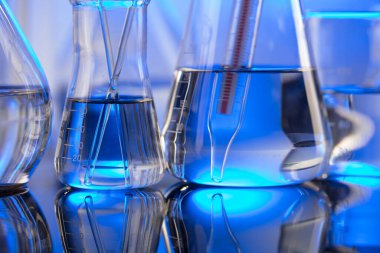 Laboratuvar araştırmaları. Mavi arka planda cam tüpler ve beherler.