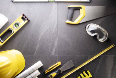 Müteahhit teması. Planlar, müteahhitin alet çantası, sarı başlık ve iftiralar. Gri karolar arka plan.